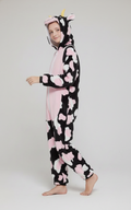 Person wearing a cow-themed onesie with pink hearts on a white background